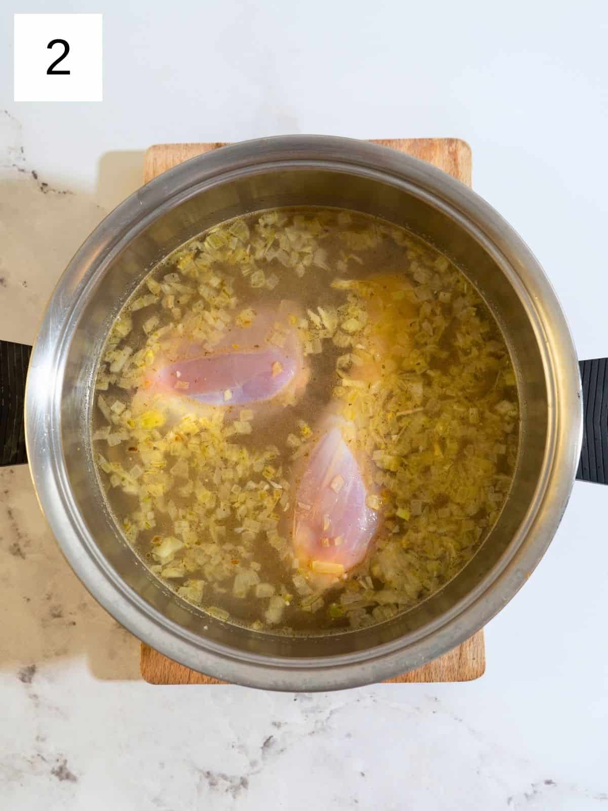 A pot filled with chicken thighs simmering in chicken broth, accompanied by a bay leaf and sprigs of thyme, as it gently cooks on the stovetop.