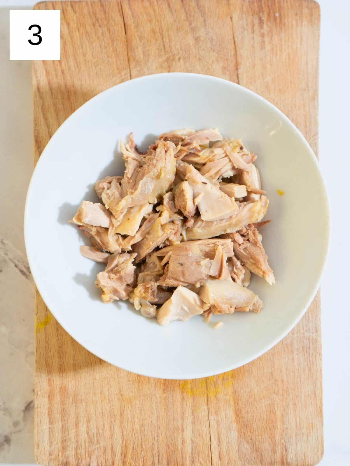 A plate of freshly shredded chicken thighs, tender and ready to be added to a simmering pot of soup.