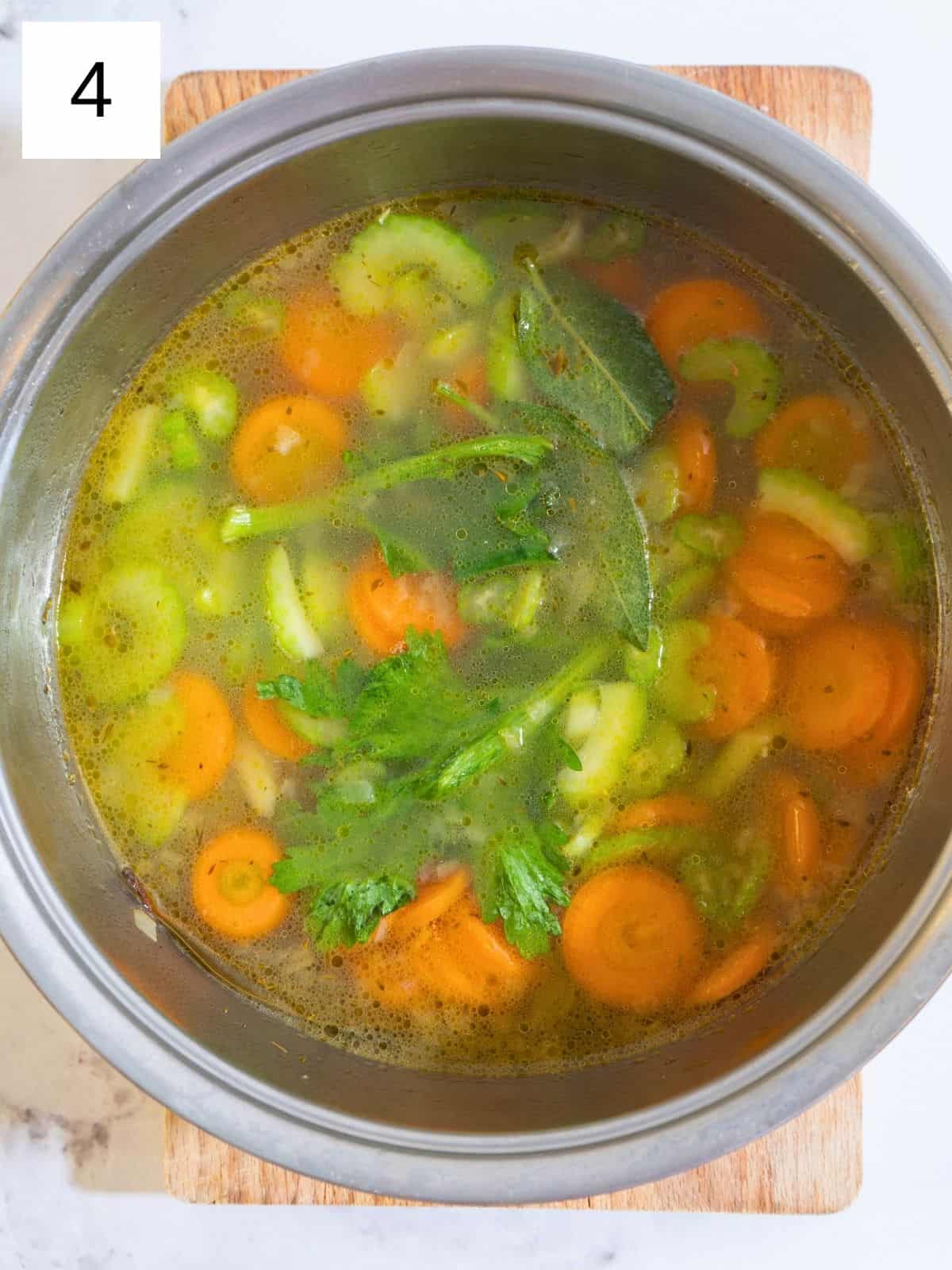 A pot of simmering soup with sliced carrots, celery, and shredded chicken just added, ready to be brought to a boil before simmering gently.