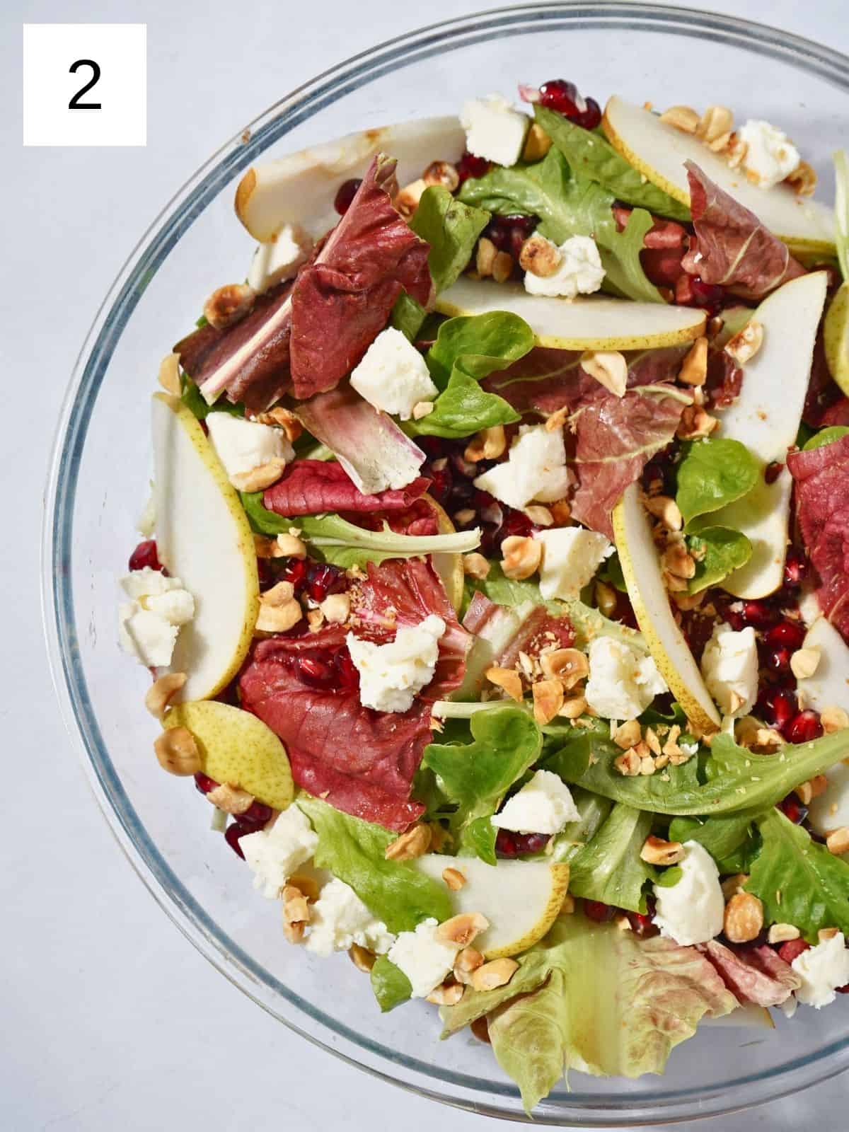 A refreshing pear and pomegranate salad topped with hazelnuts, mixed greens, goat cheese and a zesty apple cider vinegar dressing, artfully presented in a glass bowl.
