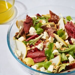 A refreshing pear and pomegranate salad topped with hazelnuts, goat cheese, mixed greens, and a zesty apple cider vinegar dressing, artfully presented in a glass bowl.