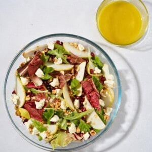 A vibrant salad in a glass bowl featuring mixed greens, goat cheese, juicy pomegranate seeds, sliced pears, crunchy hazelnuts, and a tangy apple cider vinegar dressing, beautifully mixed and ready to serve.