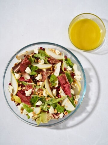 A vibrant salad in a glass bowl featuring mixed greens, goat cheese, juicy pomegranate seeds, sliced pears, crunchy hazelnuts, and a tangy apple cider vinegar dressing, beautifully mixed and ready to serve.