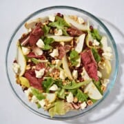 A vibrant salad in a glass bowl featuring mixed greens, goat cheese, juicy pomegranate seeds, sliced pears, and crunchy hazelnuts, perfect for a refreshing and healthy dish.