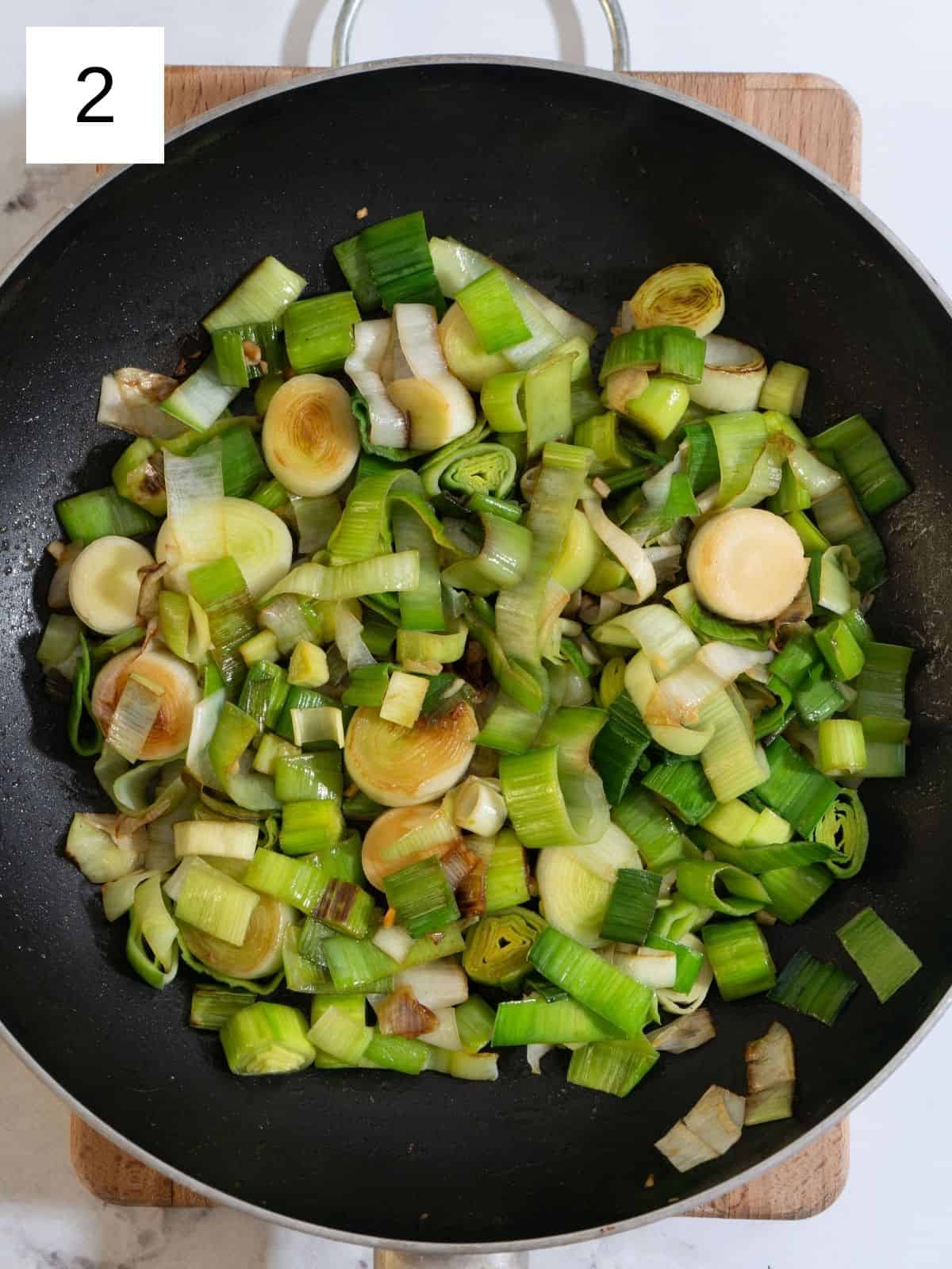 Golden-browned chicken breast in a skillet with sliced leeks and minced garlic added.