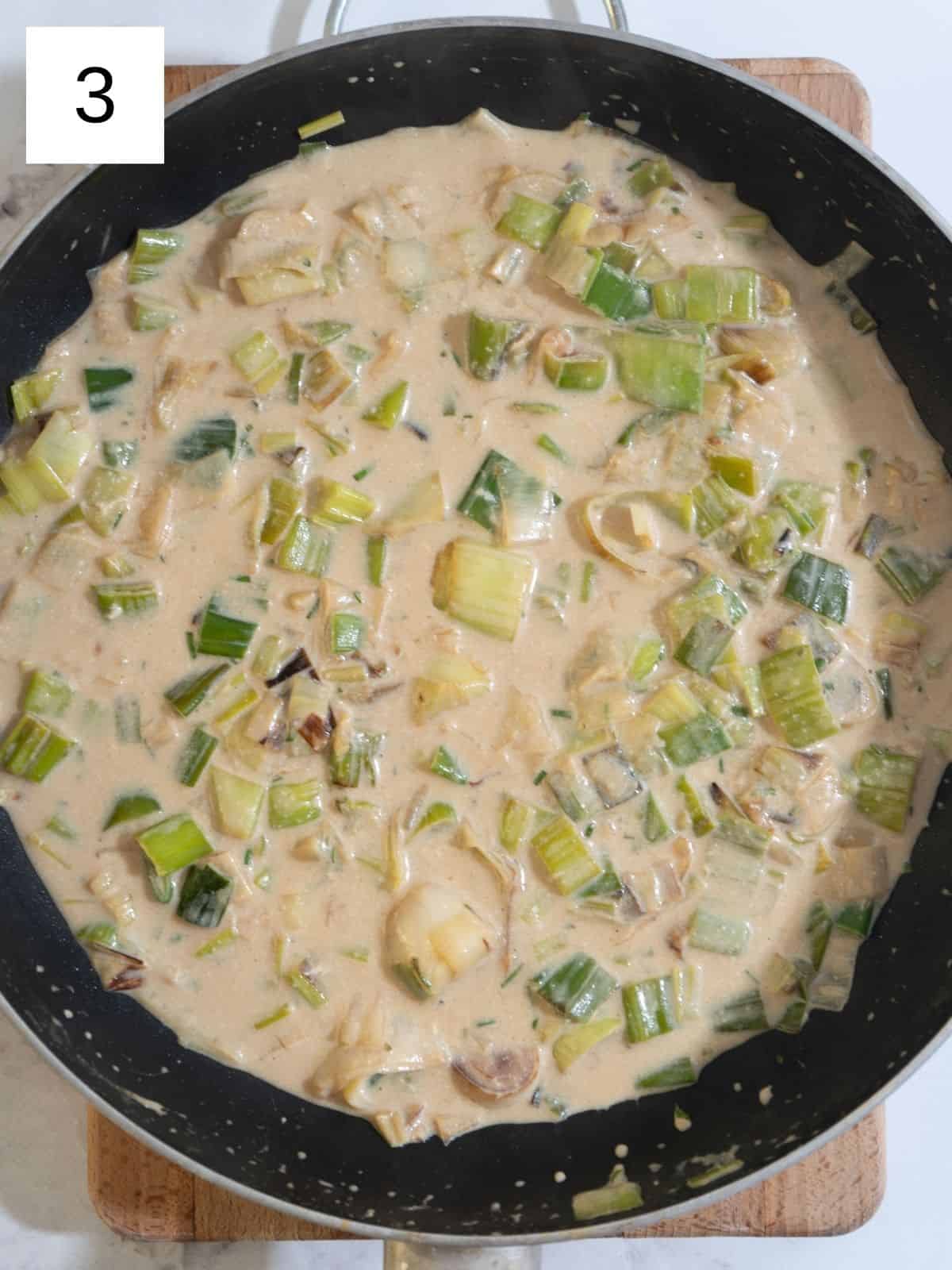 Chicken breast in a skillet with sliced leeks, mixed with chicken broth and coconut milk, ready to simmer into a flavorful dish.