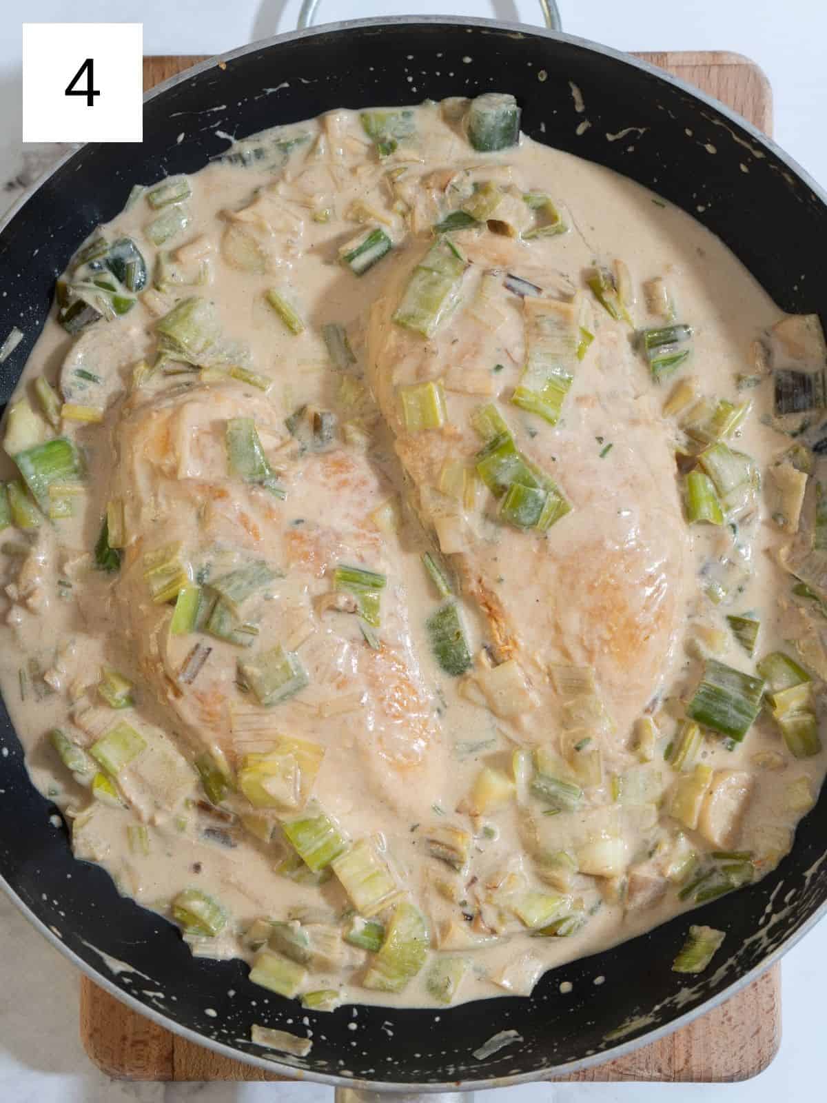 Chicken breast in a skillet, with leeks, garlic, chicken broth, and coconut milk.