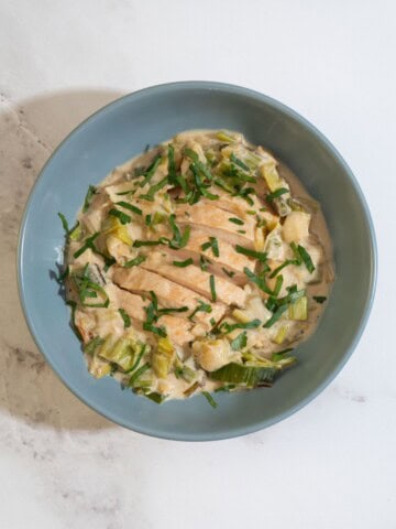 Stovetop leeks with tender chicken in a bowl, topped with fresh herbs for a flavorful, low histamine meal.