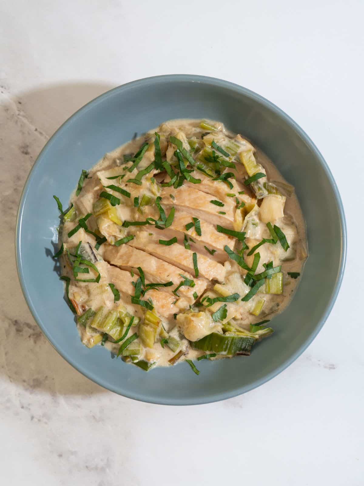 Stovetop leeks with tender chicken in a bowl, topped with fresh herbs for a flavorful, low histamine meal.