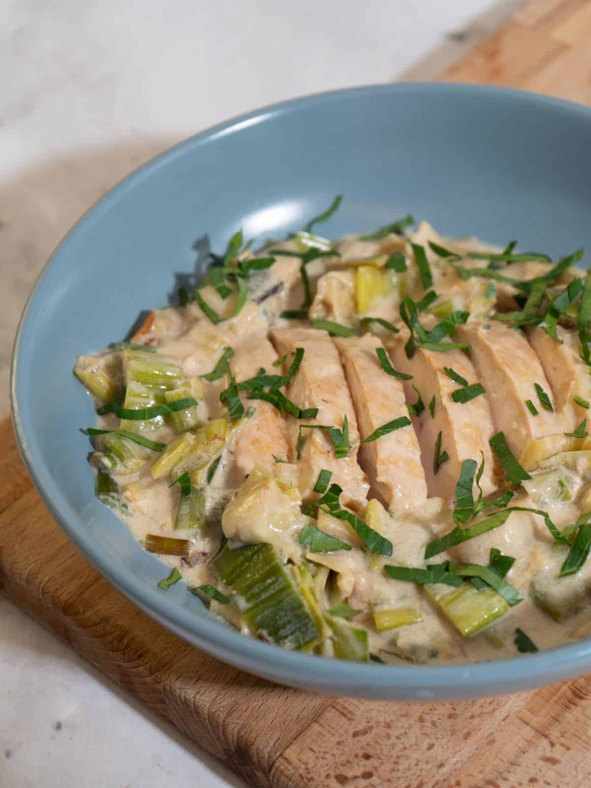 A comforting bowl of stovetop leeks with chicken, garnished with fresh herbs.