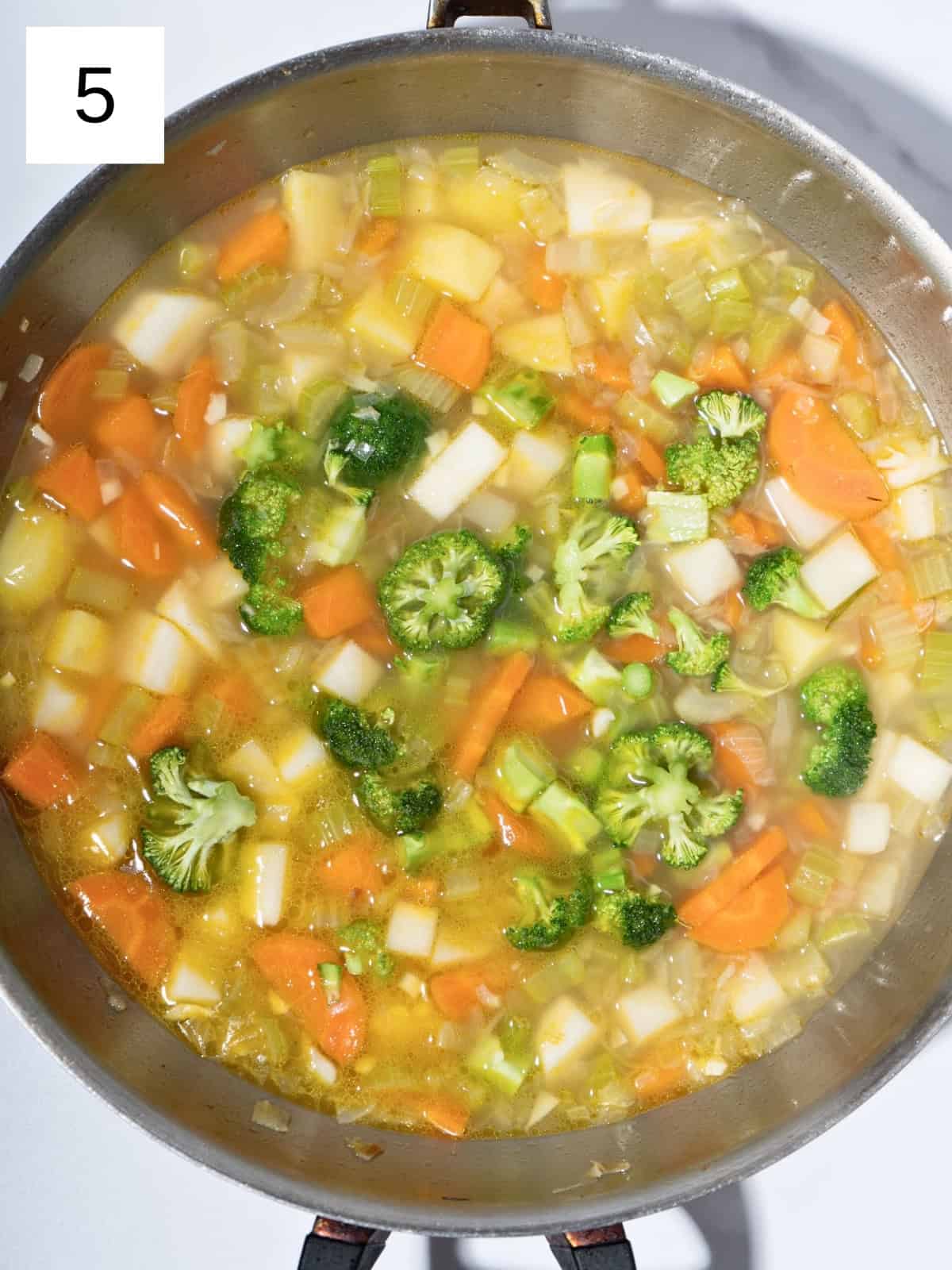 Chopped vegetables stirred together in a pot, with vegetable broth poured in and brought to a boil to create a savory vegetable stew.