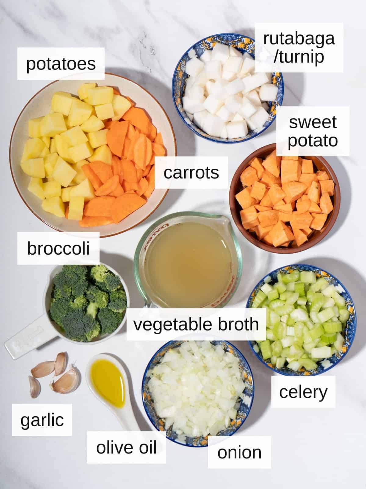 Ingredients for vegetable stew, including potatoes, carrots, rutabaga, sweet potato, broccoli, vegetable broth, celery, garlic, olive oil. and onion.