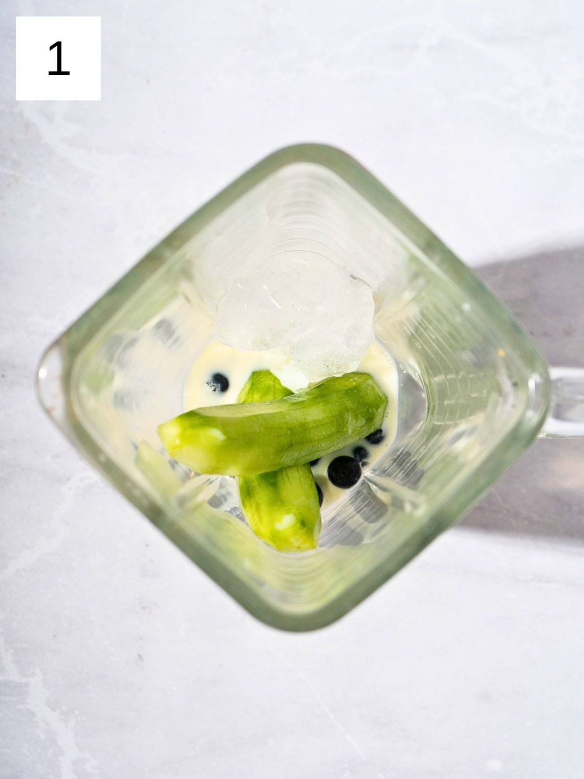 A mixture of blueberries, cucumber halves, and milk in a blender.