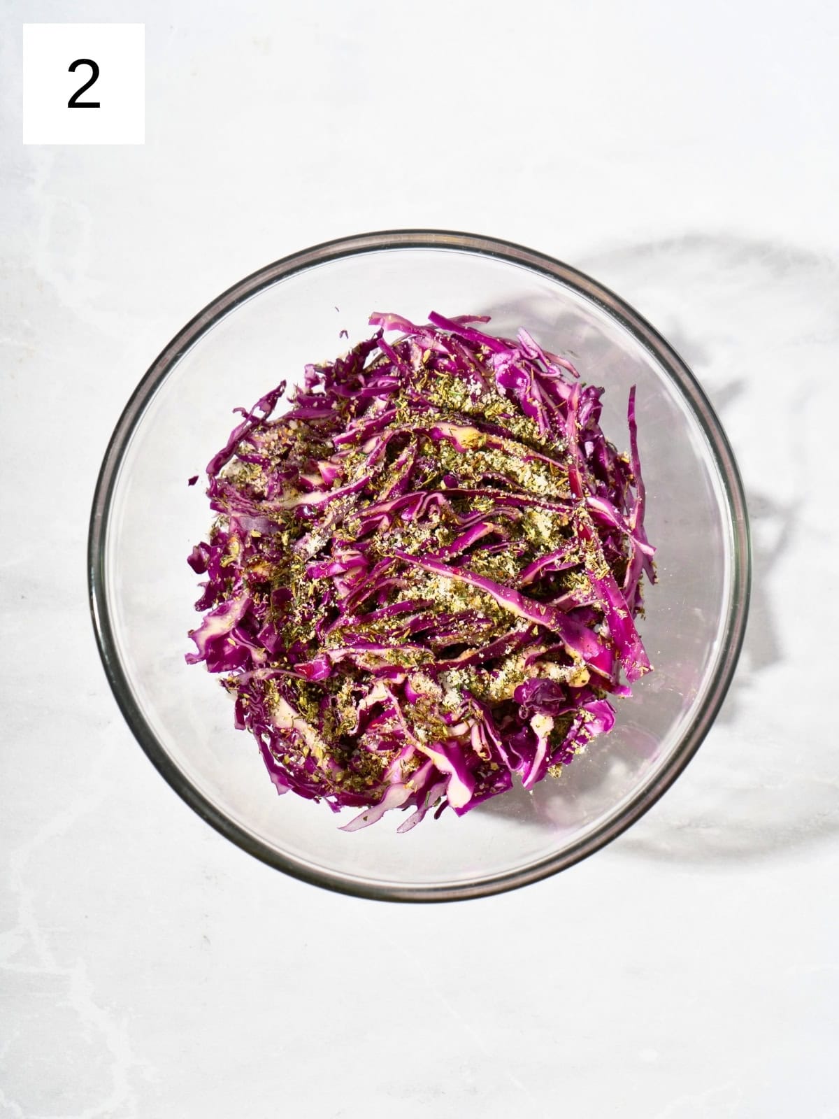 Thinly sliced purple cabbage, drizzled with olive oil, salt, and Italian seasoning blend, in a bowl.