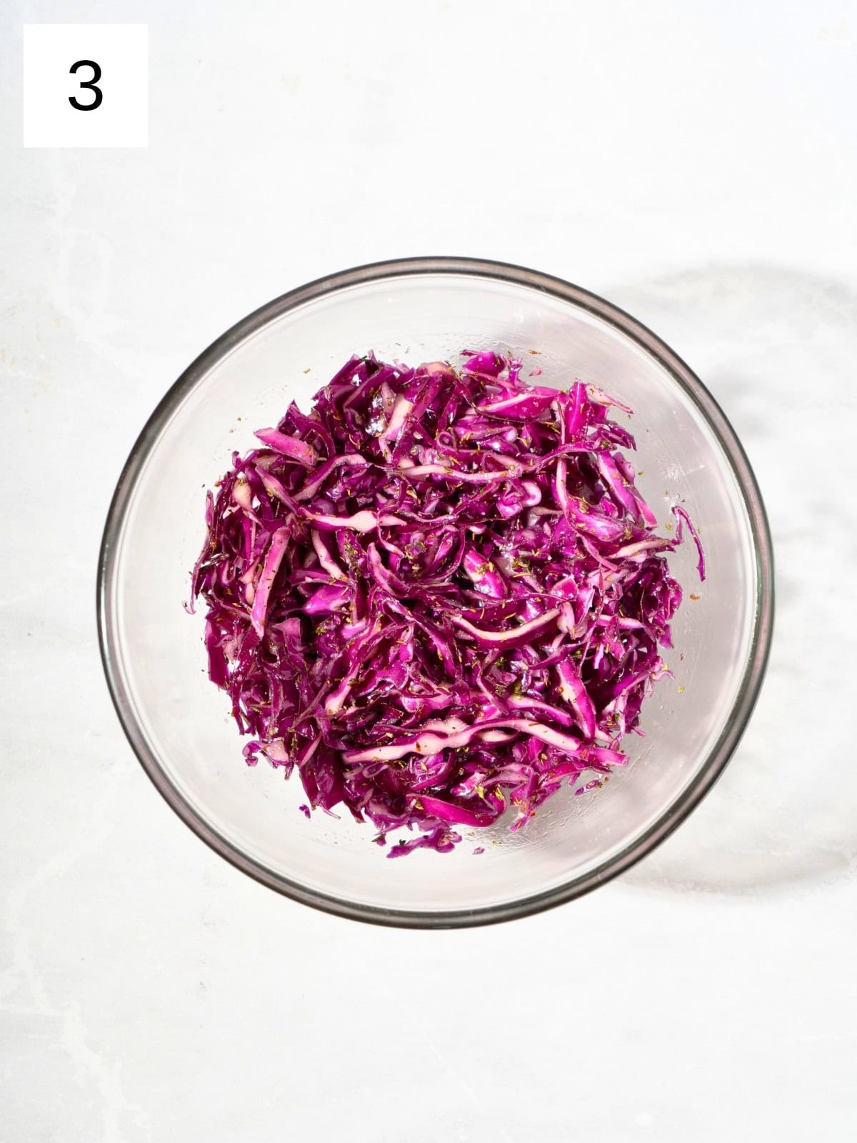 Thinly sliced purple cabbage, coated with olive oil, salt, and Italian seasoning blend, in a bowl.