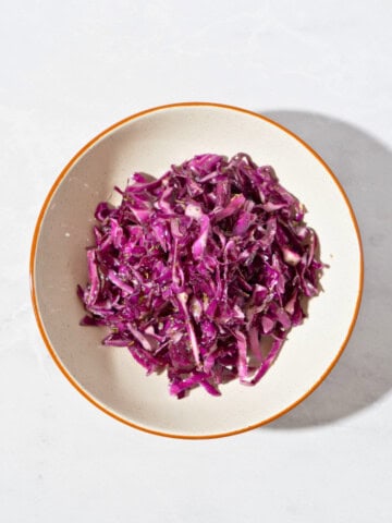 Colorful cabbage salad coated with Italian seasoning dressing, showcasing thinly sliced purple cabbage and a drizzle of olive oil, served in a bowl.