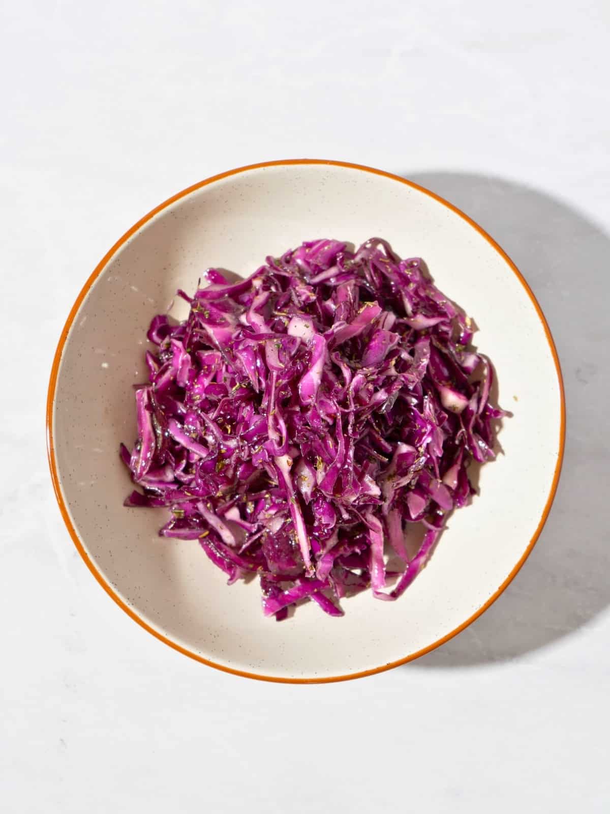 Colorful cabbage salad coated with Italian seasoning dressing, showcasing thinly sliced purple cabbage and a drizzle of olive oil, served in a bowl.