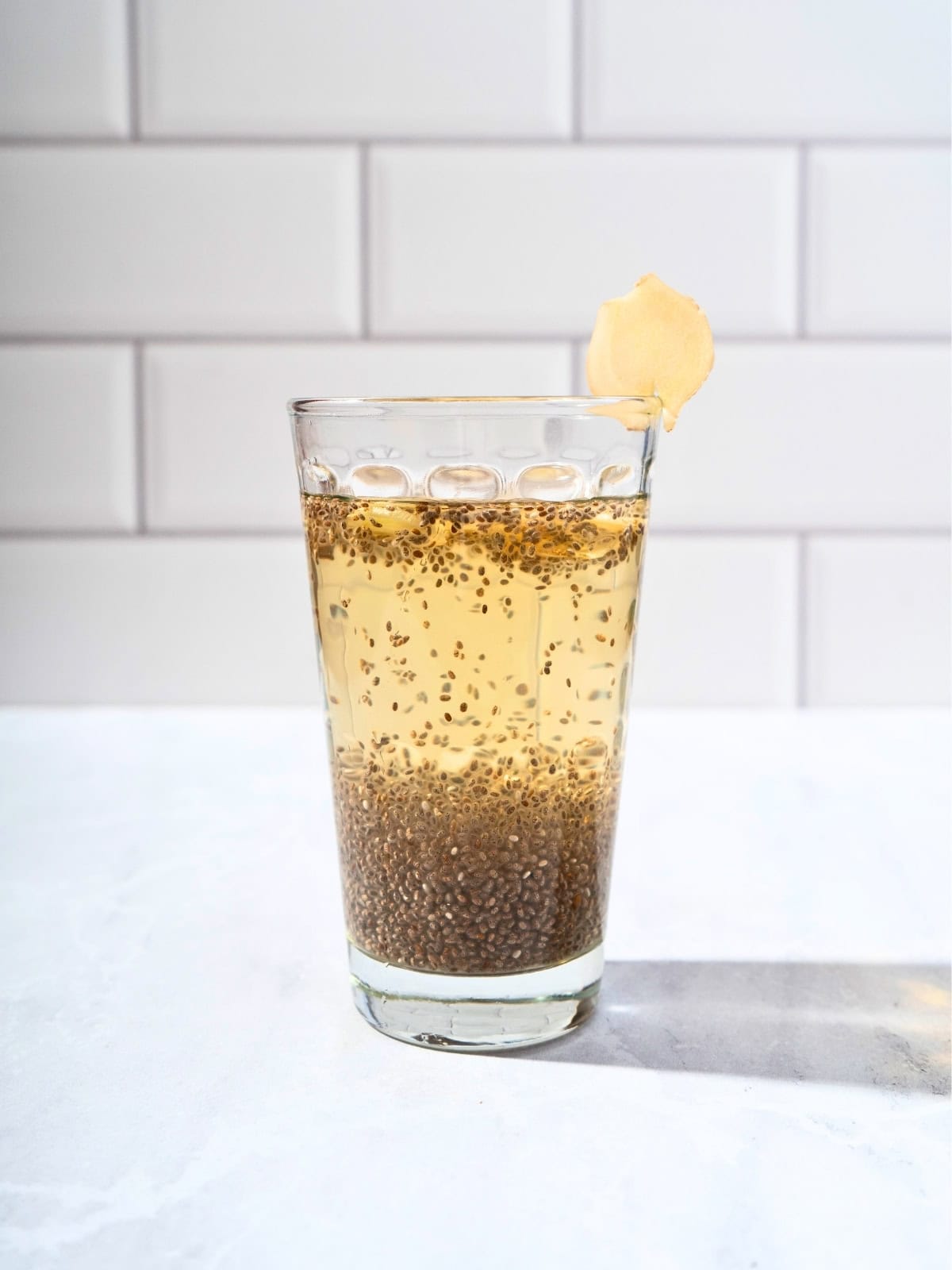 Glass of refreshing chia apple juice garnished with fresh ginger slices, showcasing a healthy and vibrant beverage.