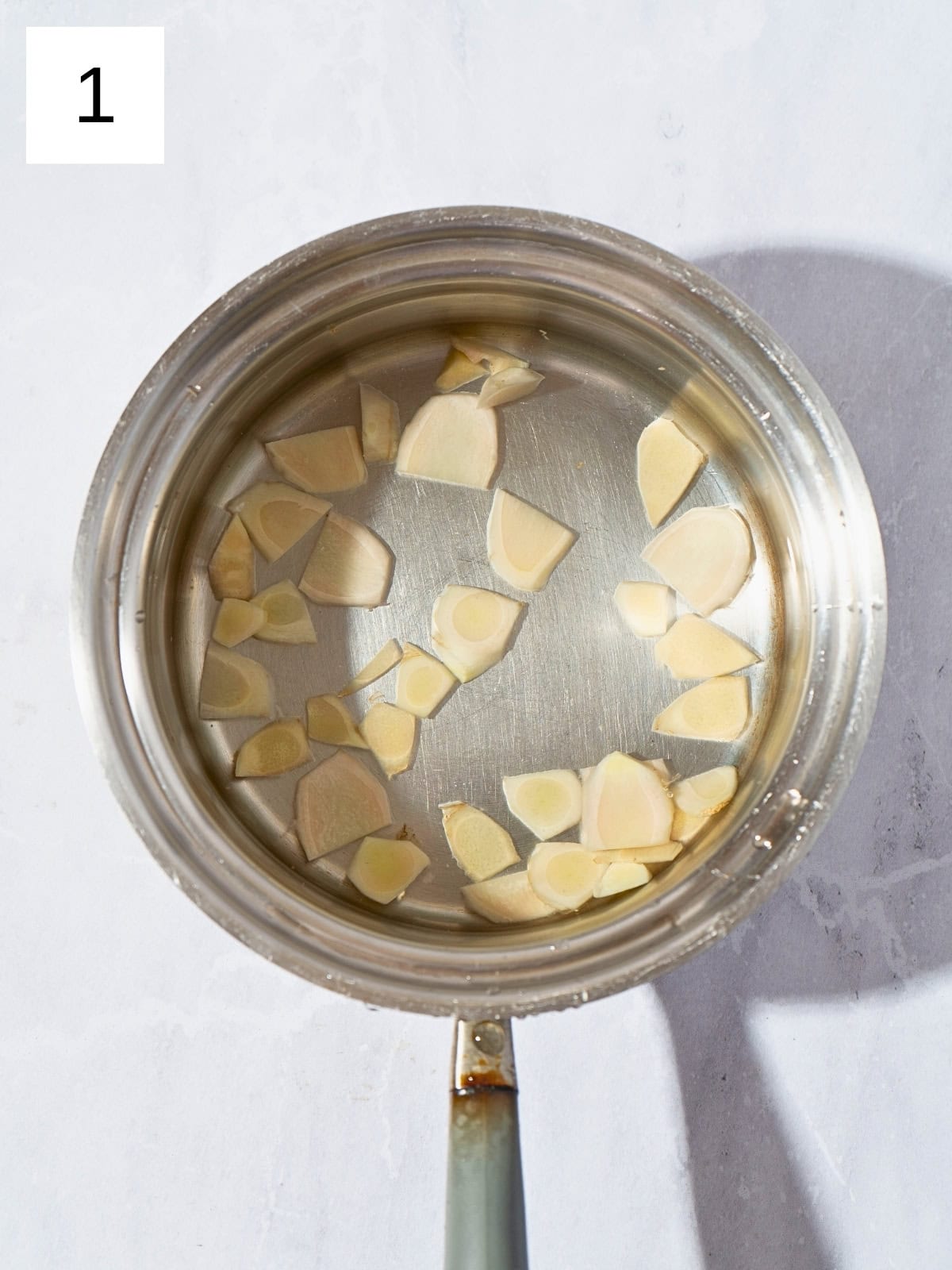 Fresh ginger slices in a saucepan filled with boiled water.