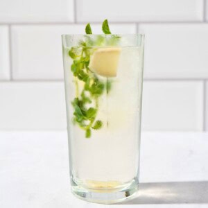 A tall glass of refreshing iced ginger mint tea garnished with fresh mint leaves, ginger, and ice cubes.