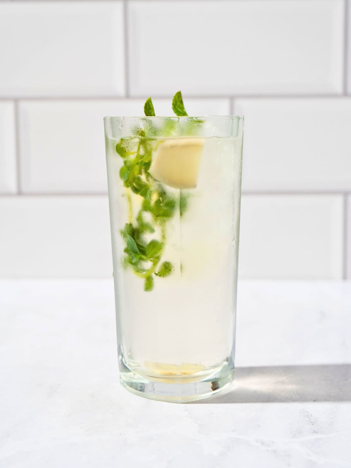 A tall glass of refreshing iced ginger mint tea garnished with fresh mint leaves, ginger, and ice cubes.