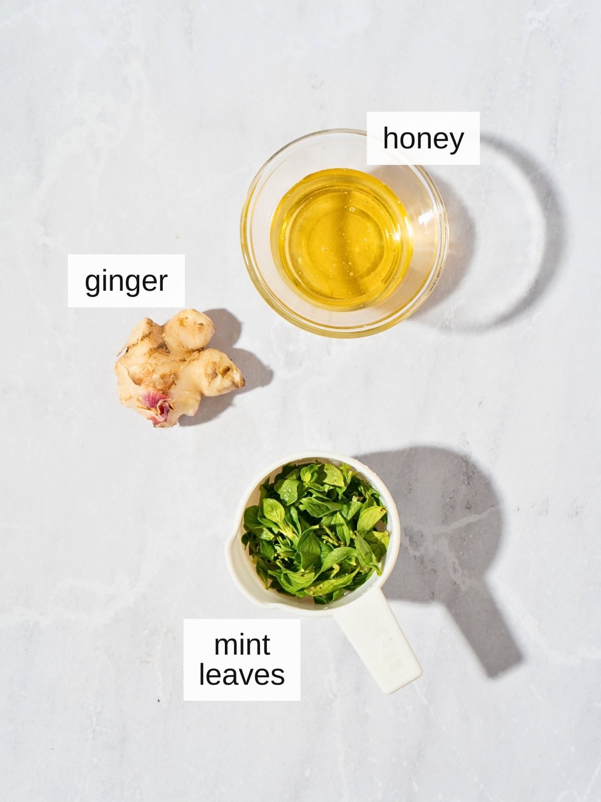 Ingredients for iced ginger mint tea, including honey, fresh ginger, and fresh mint leaves.