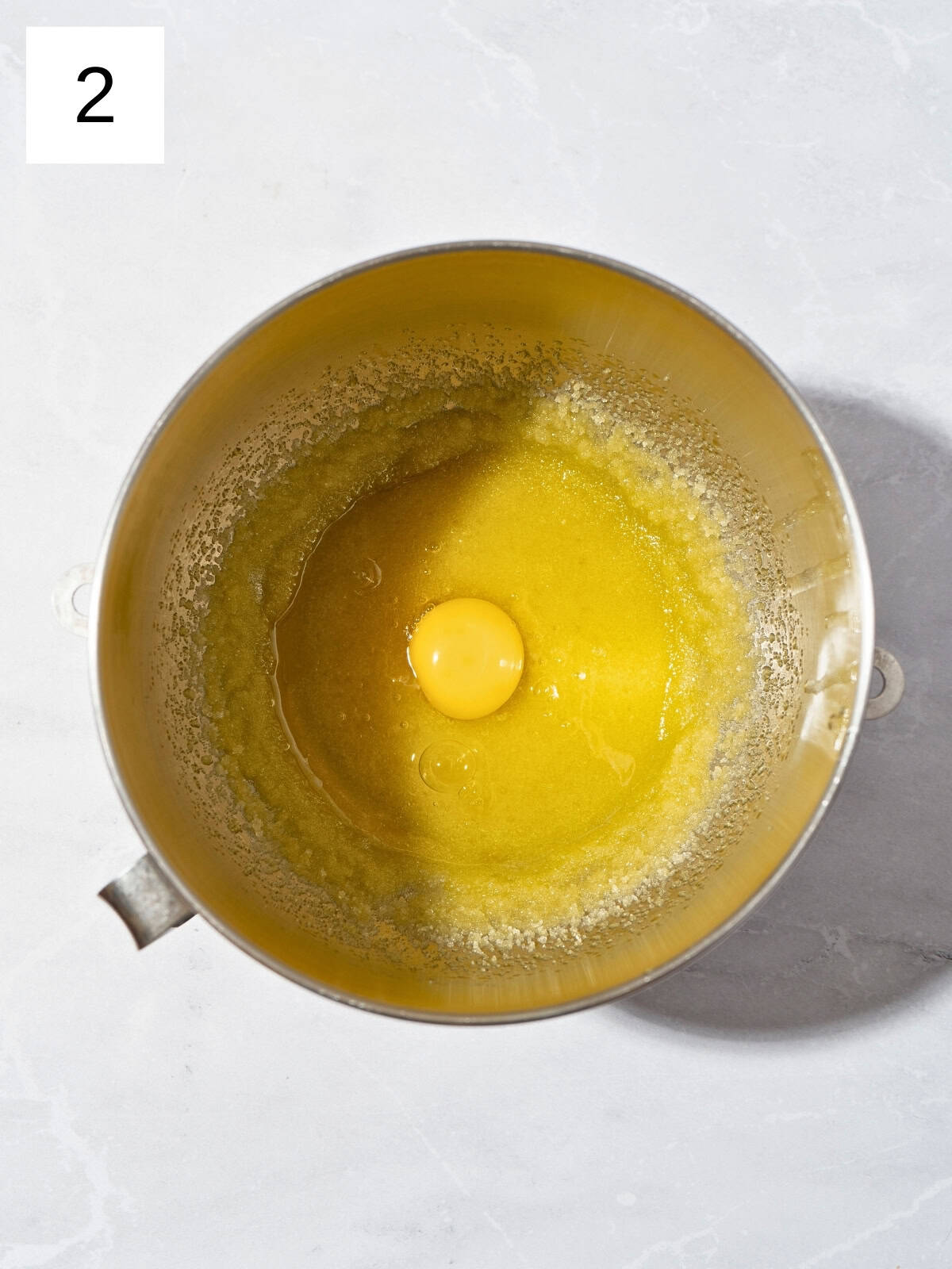 A mixture of olive oil and granulated sugar with egg in a large mixing bowl.