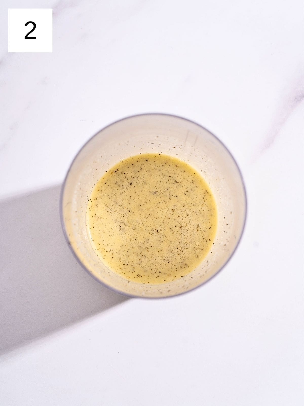 A food processor bowl filled with a mixture of garlic salad dressing.