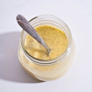 A glass container filled with creamy garlic salad dressing, showcasing a smooth texture and fresh ingredients.