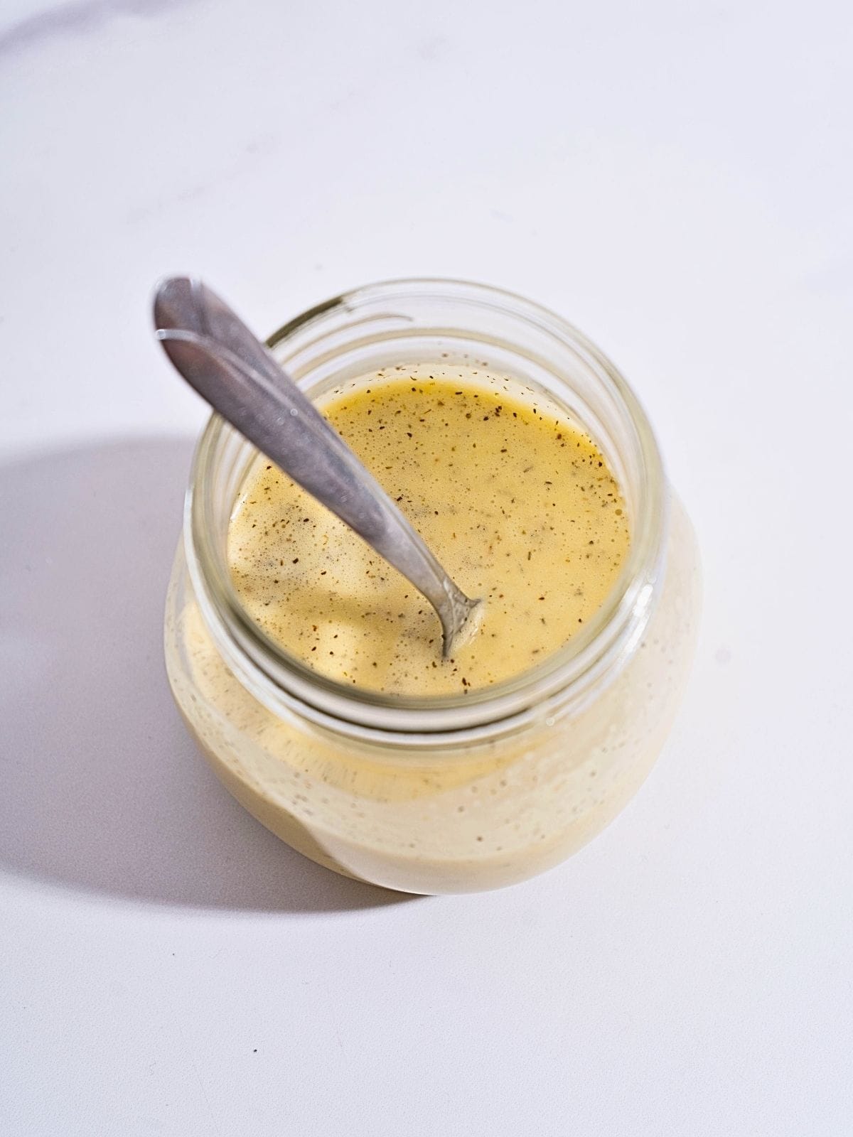 A glass container filled with creamy garlic salad dressing, showcasing a smooth texture and fresh ingredients.