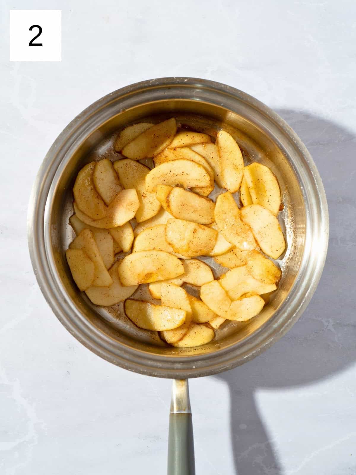 Stewed sliced apples with sugar and ground cinnamon in a saucepan.