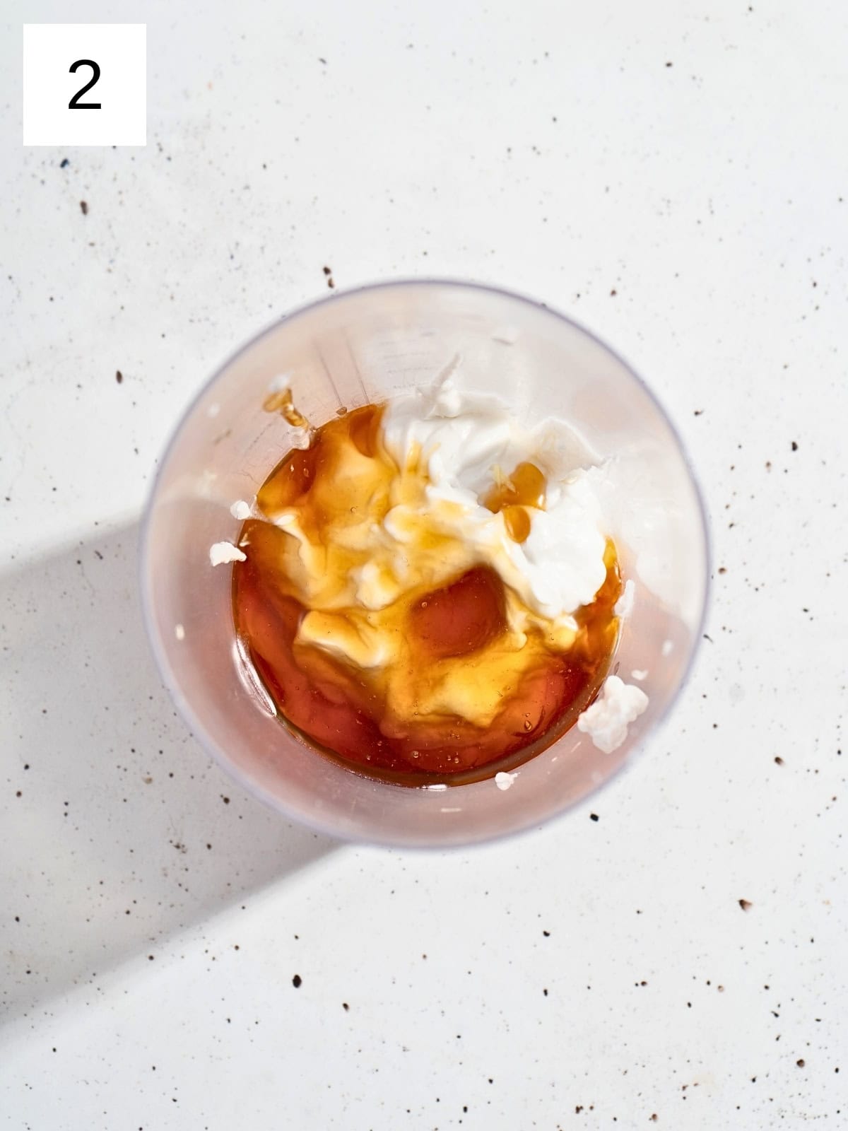 A mixture of grated ginger and garlic, maple syrup, coconut cream, salt, and apple cider vinegar in a food processor.