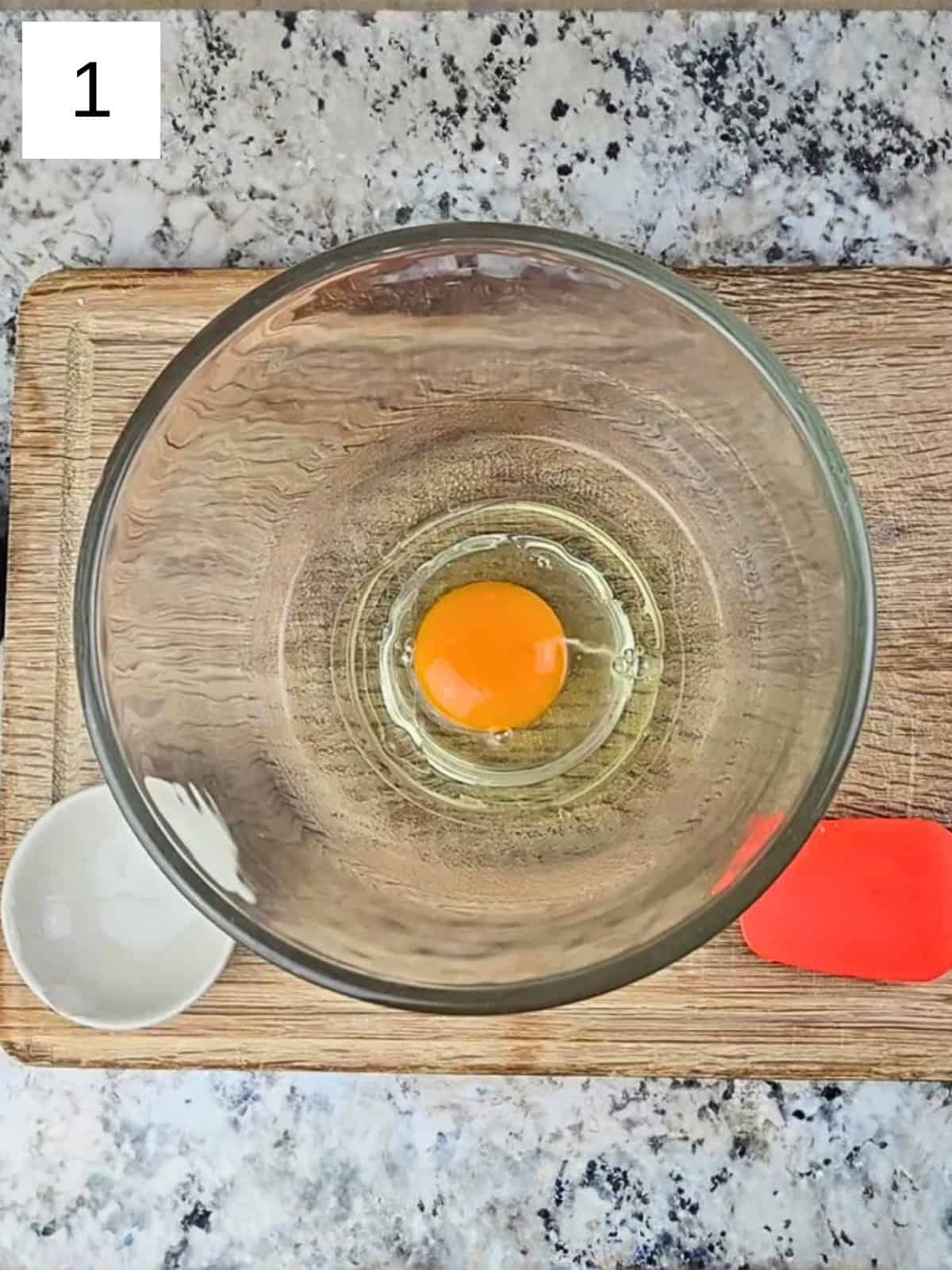 One whole egg and an oil in a glass mixing bowl.