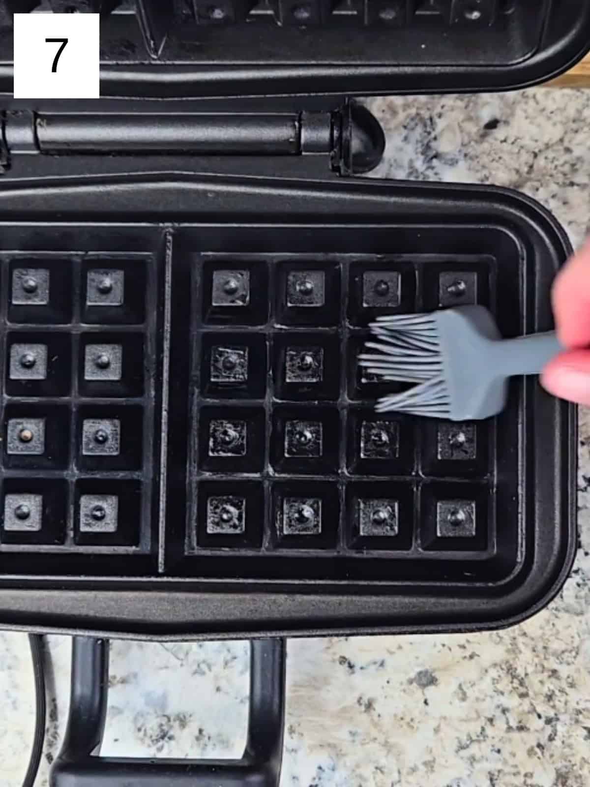 A preheated waffle maker being brushed with oil before cooking.