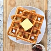 Stack of golden waffles on a plate topped with a pat of butter.