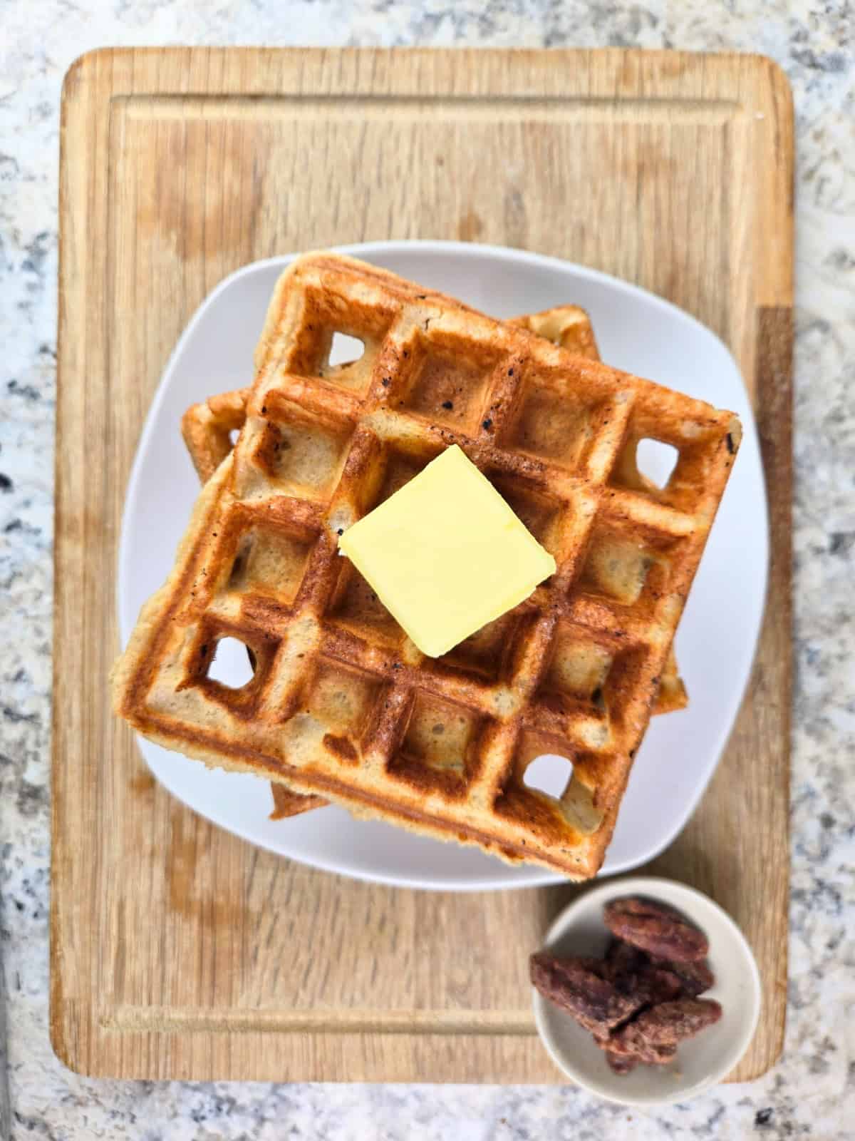 Stack of golden waffles on a plate topped with a pat of butter.