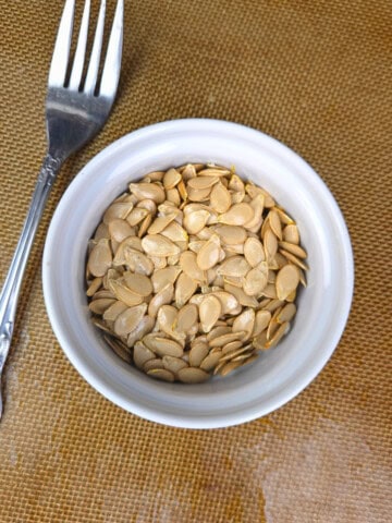 A small bowl filled with golden-brown, crispy roasted squash seeds, perfect as a healthy low-histamine snack or salad topper.