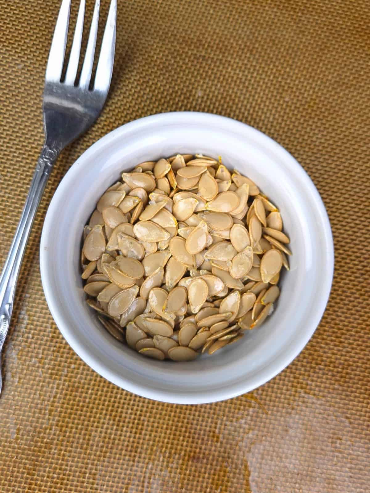A small bowl filled with golden-brown, crispy roasted squash seeds, perfect as a healthy low-histamine snack or salad topper.