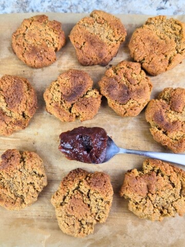 Freshly baked vanilla almond cookies on a wooden chopping board with a spoonful of sauce alongside.