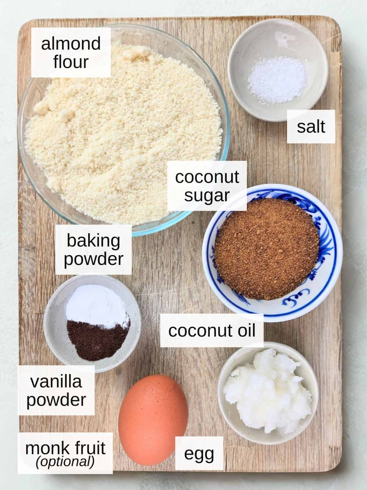 ingredients for vanilla almond cookies, including baking powder, coconut sugar, monk fruit powder, almond flour, sea salt, egg, coconut oil, and vanilla powder.