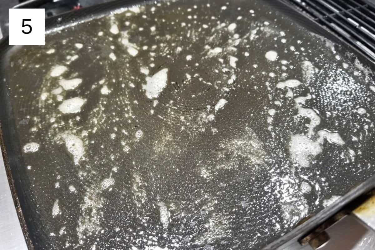 Pancake batter cooking in a frying pan, beginning to set and form bubbles for fluffy homemade pancakes.