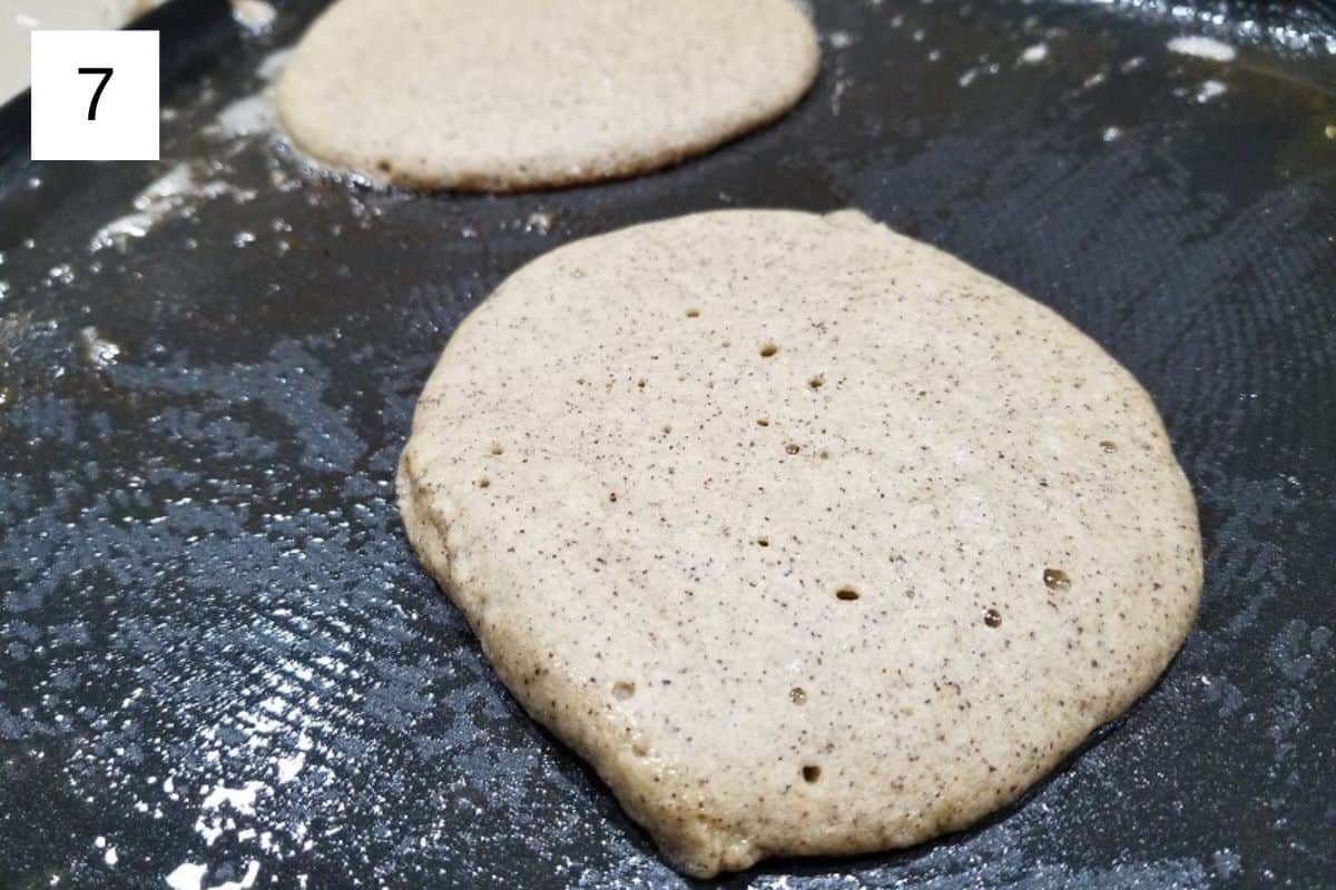 Pancake batter cooking in a frying pan, beginning to set and form bubbles for fluffy homemade pancakes.
