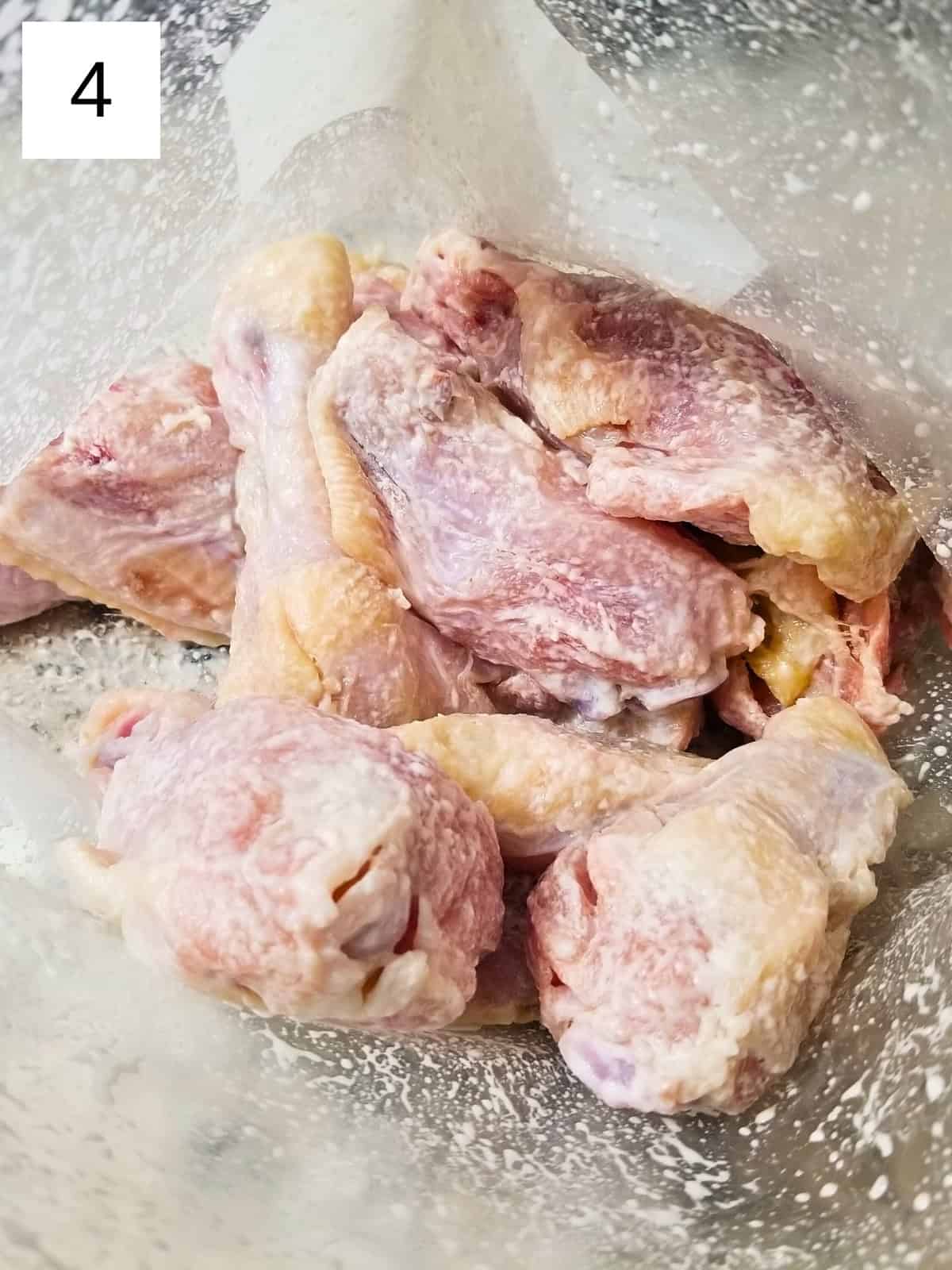 Raw chicken pieces in a zip-top freezer bag coated with salt and baking powder seasoning.