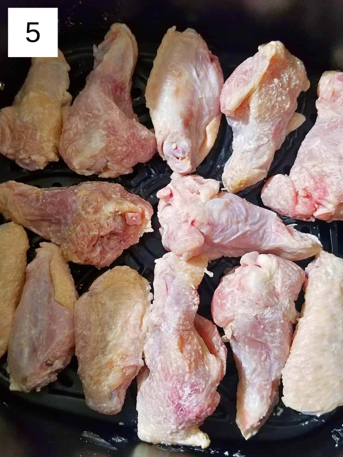Raw chicken pieces seasoned and placed in an air fryer.