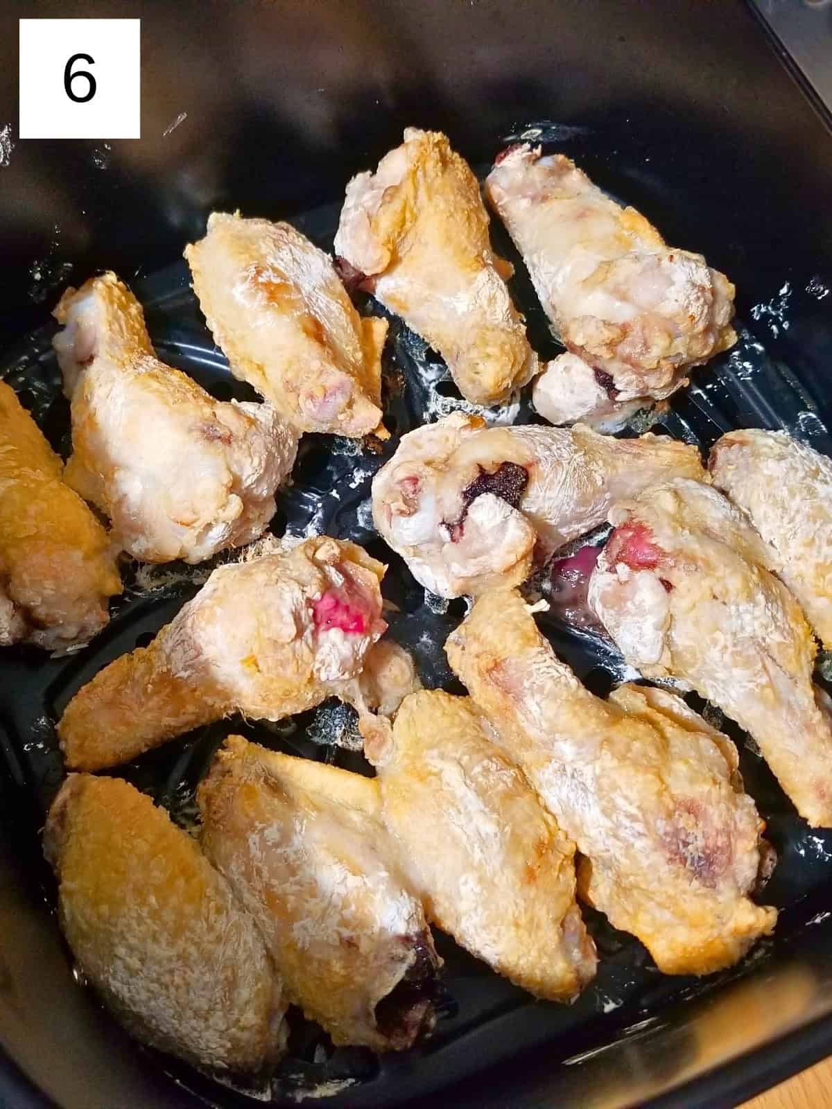 Half-cooked chicken pieces in an air fryer.