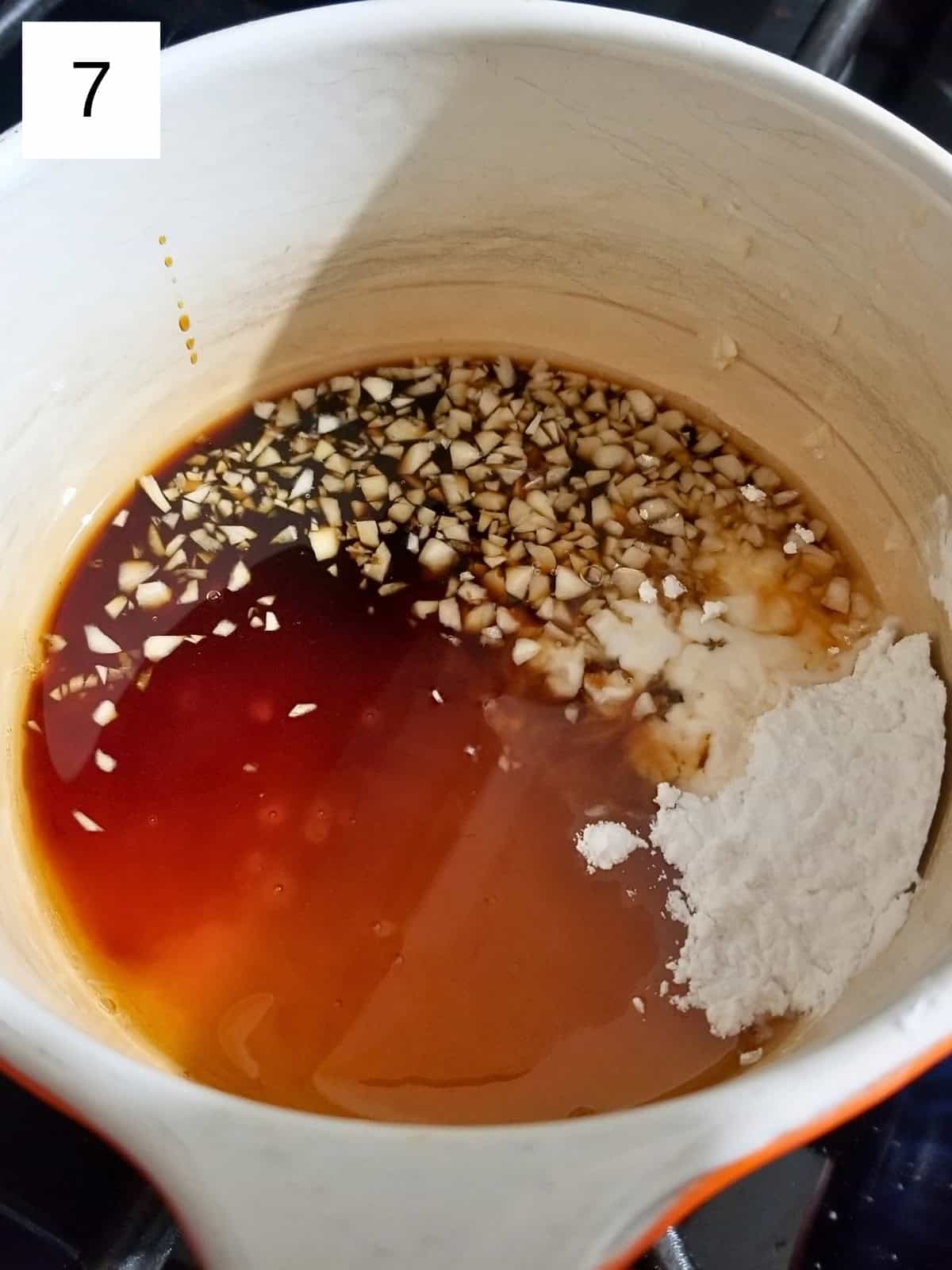 A mixture of honey, minced garlic, water, tapioca starch, vinegar, and coconut aminos in a saucepan.