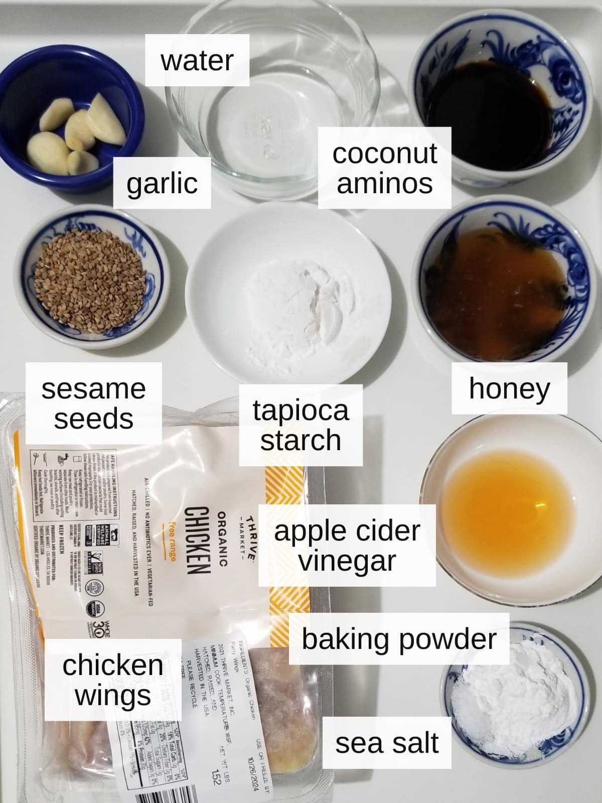 Ingredients for honey garlic chicken wings, including coconut aminos, water, garlic, honey, tapioca starch, apple cider vinegar, sesame seeds, baking powder, sea salt, and chicken wings.