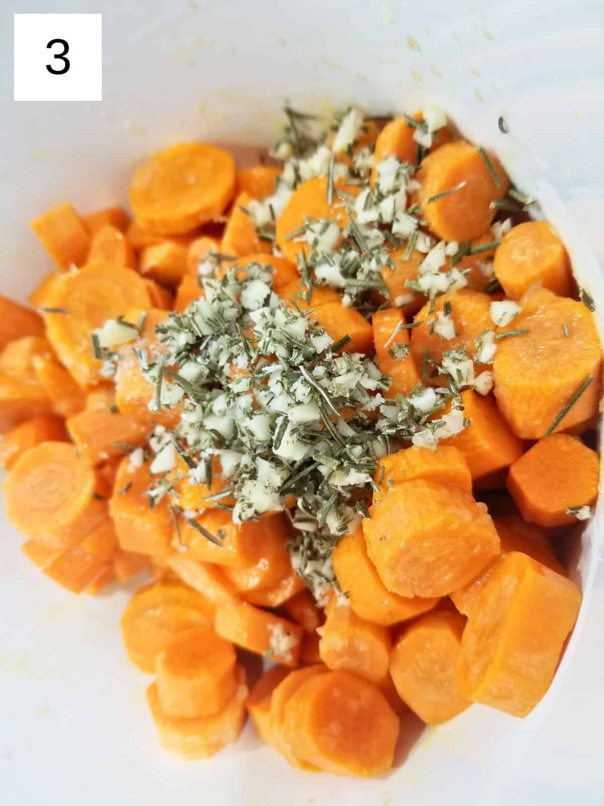 slices of carrots with oil, maple syrup, minced garlic, dried rosemary, salt, and sumac in a bowl.