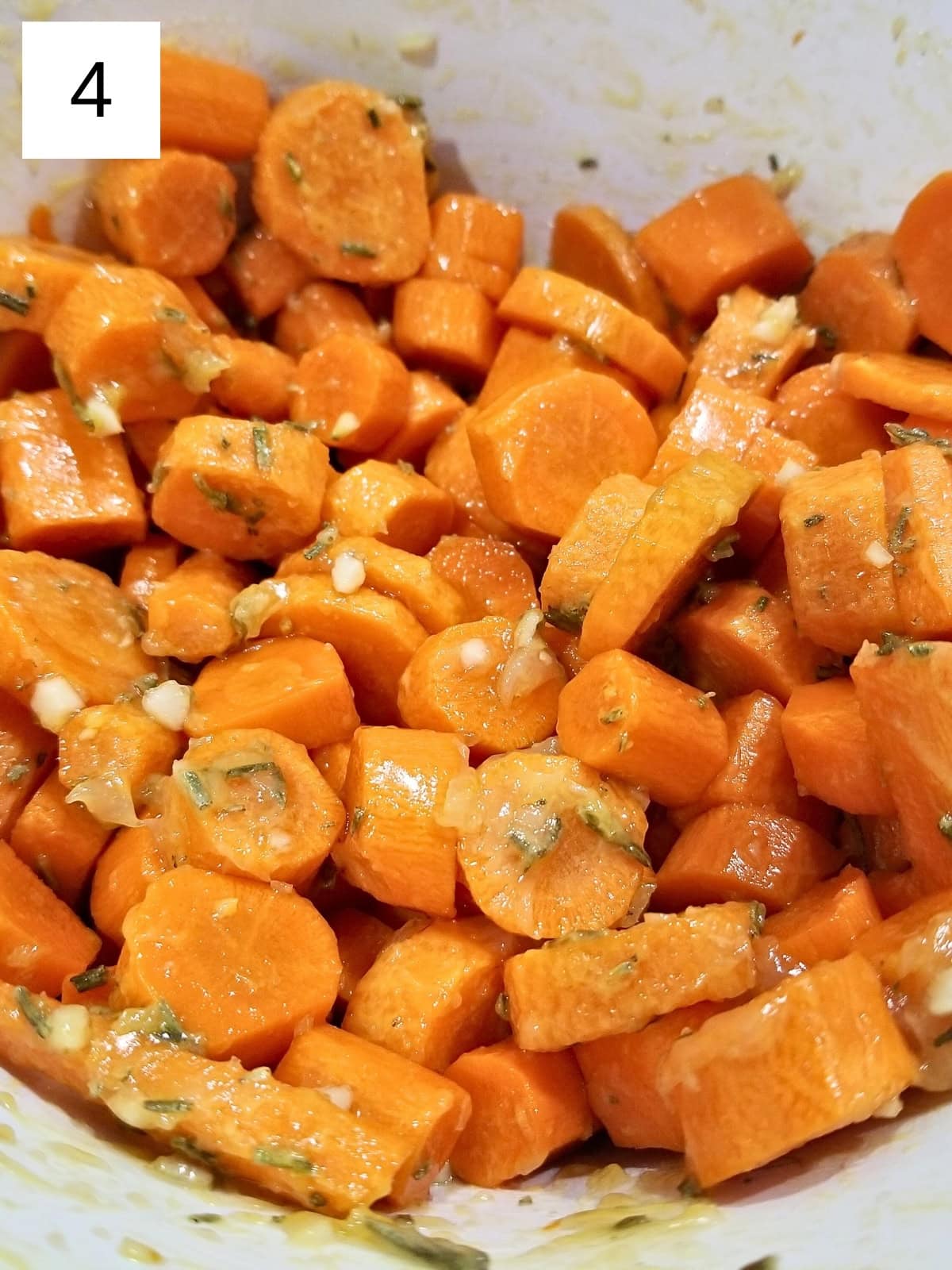 slices of carrots with oil, maple syrup, minced garlic, dried rosemary, salt, and sumac in a bowl.