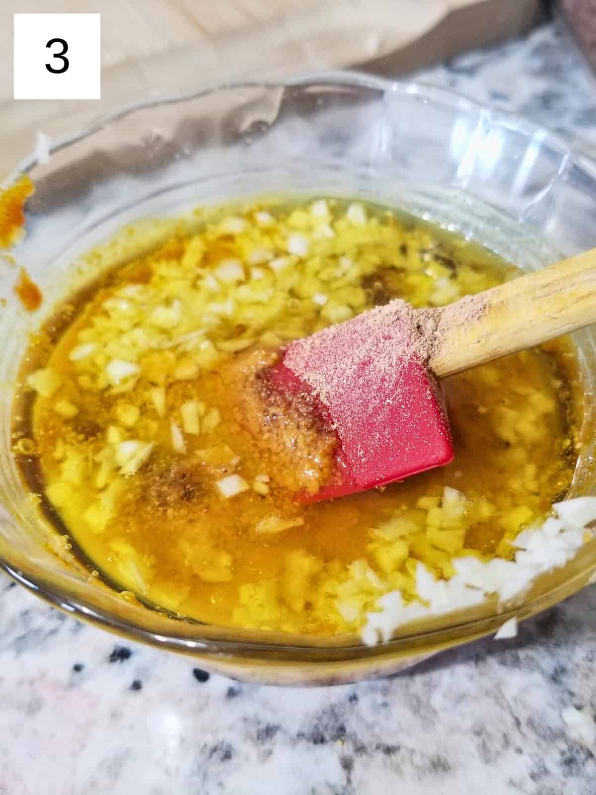 A mixture of coconut oil, honey, turmeric paste, mustard powder, amchur powder, minced garlic, and salt in a glass bowl.
